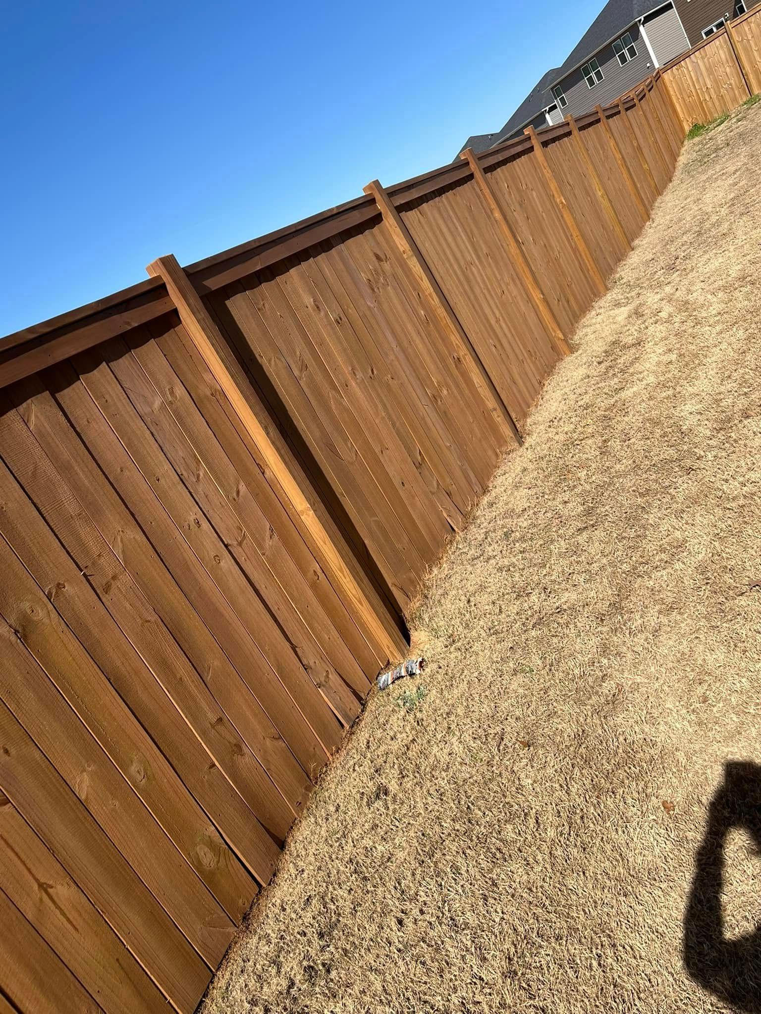 Brown wooden fence next to a pile of gravel against a clear blue sky.