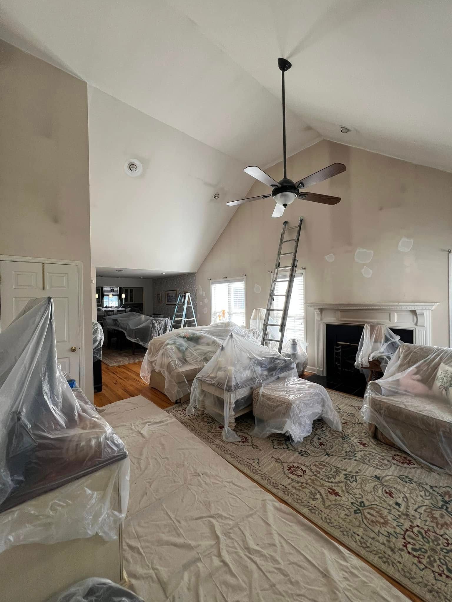 Living room during renovation; furniture covered, ladder against wall, neutral color scheme.