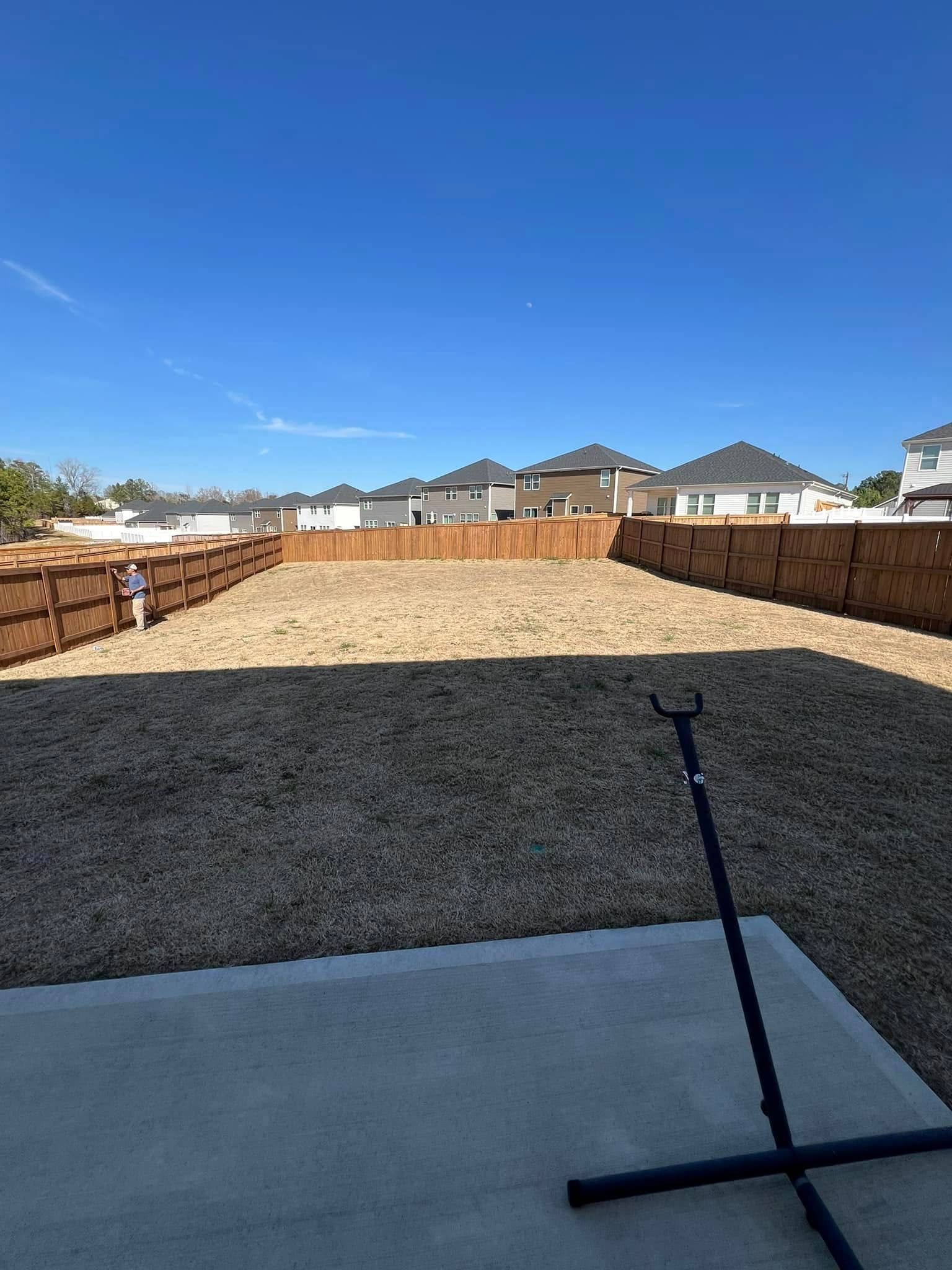 Empty backyard with gravel and wooden fence under a blue sky.