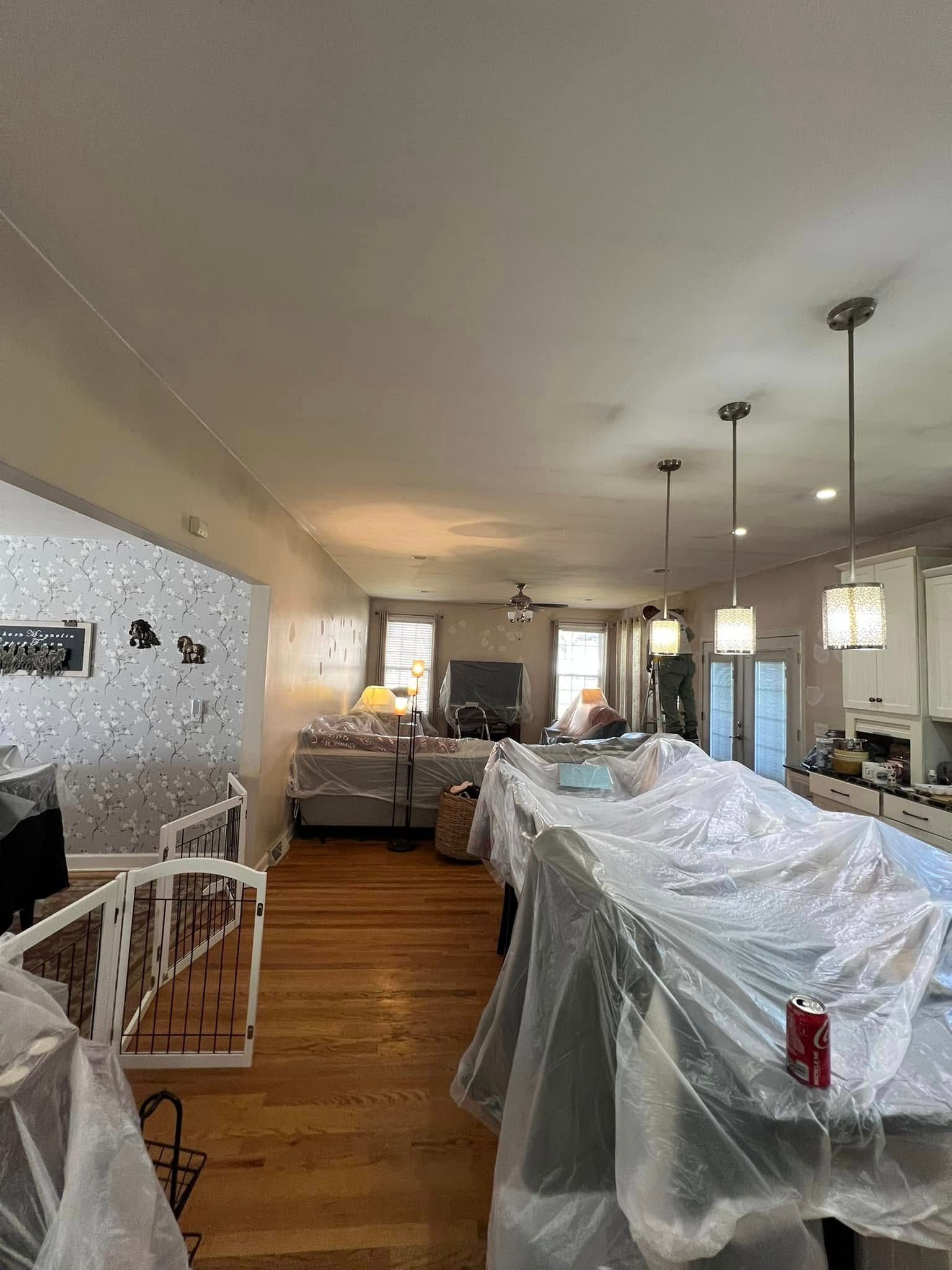 Interior view of a home, wooden floors, kitchen with island covered in plastic, walls painted, and some baby gates.