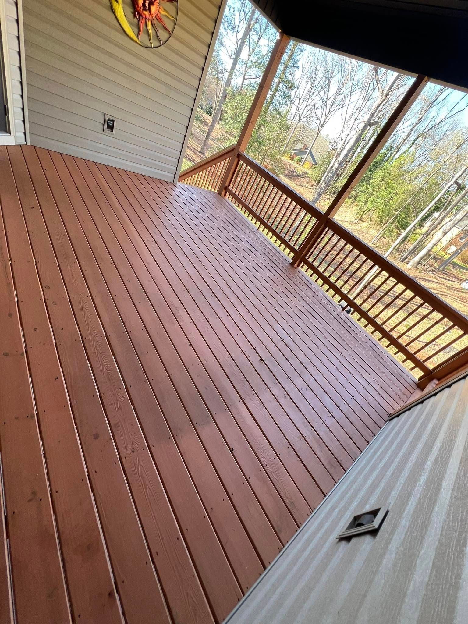 Wooden deck with brown railings, overlooking a wooded area, tan siding.