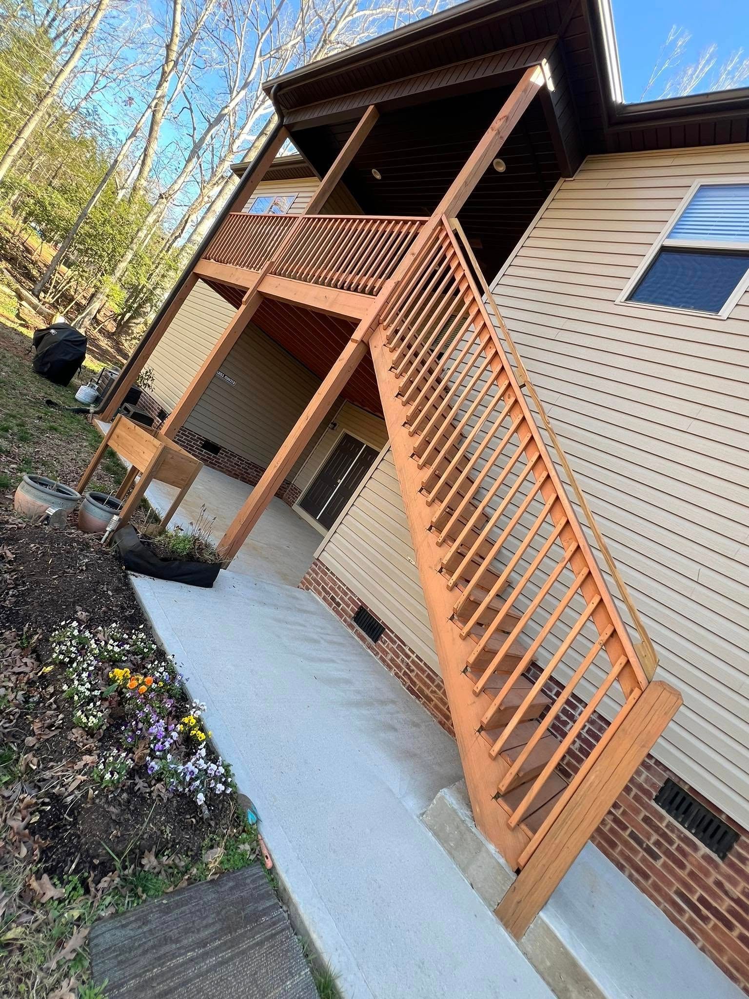 Two-story house with wooden deck and stairs, tan siding, brick accents, and concrete walkway.