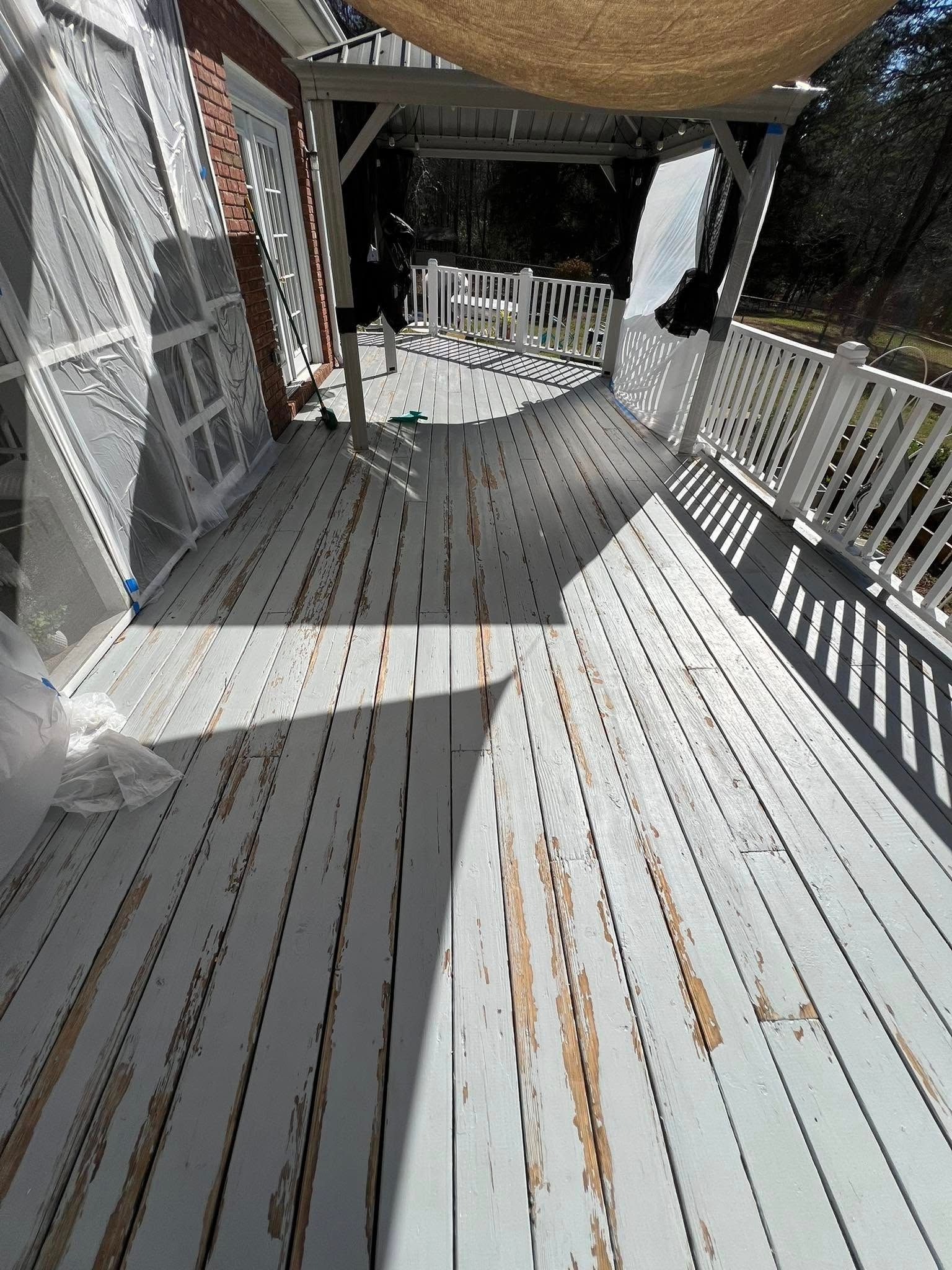 A white wooden deck with peeling paint and sunlight, surrounded by a white railing and partially covered.