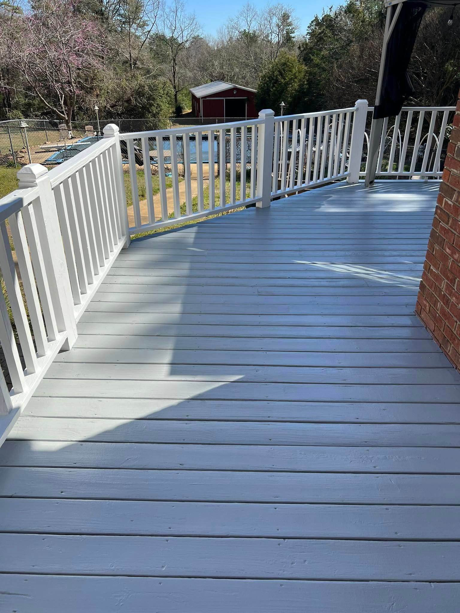 Gray painted wooden deck with white railing, brick wall, and distant red shed.