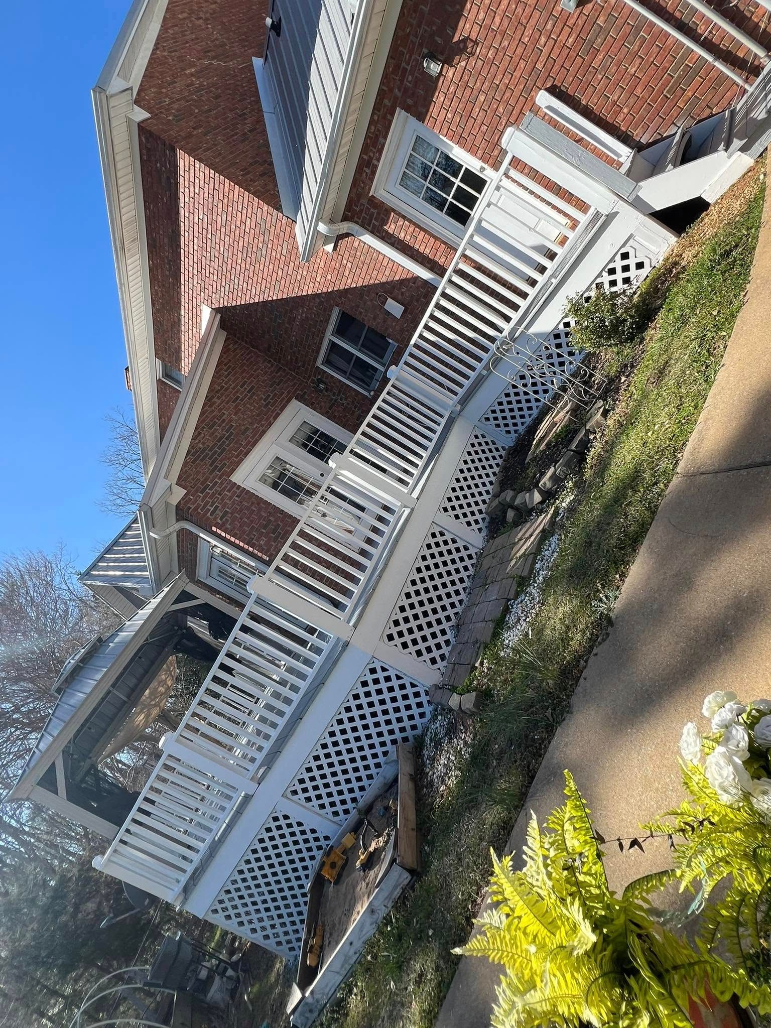Brick building with white porch, latticework, and a clear blue sky.