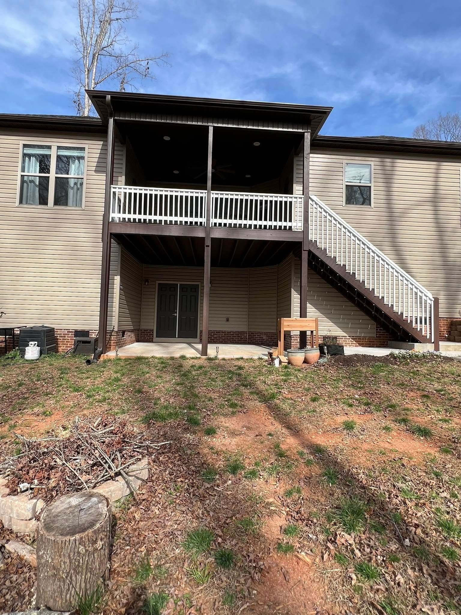 Back of house with screened porch, stairs, tan siding, brown trim, and sloped yard.