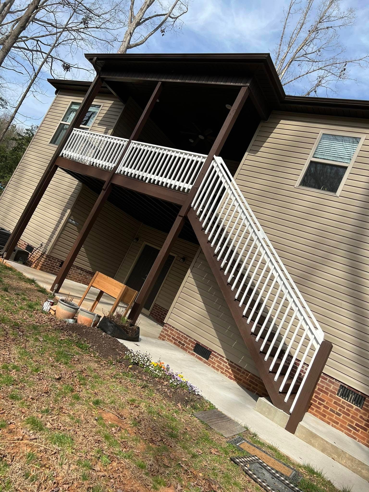 Exterior of a two-story brick house with a brown deck, white railing, and outdoor stairs.