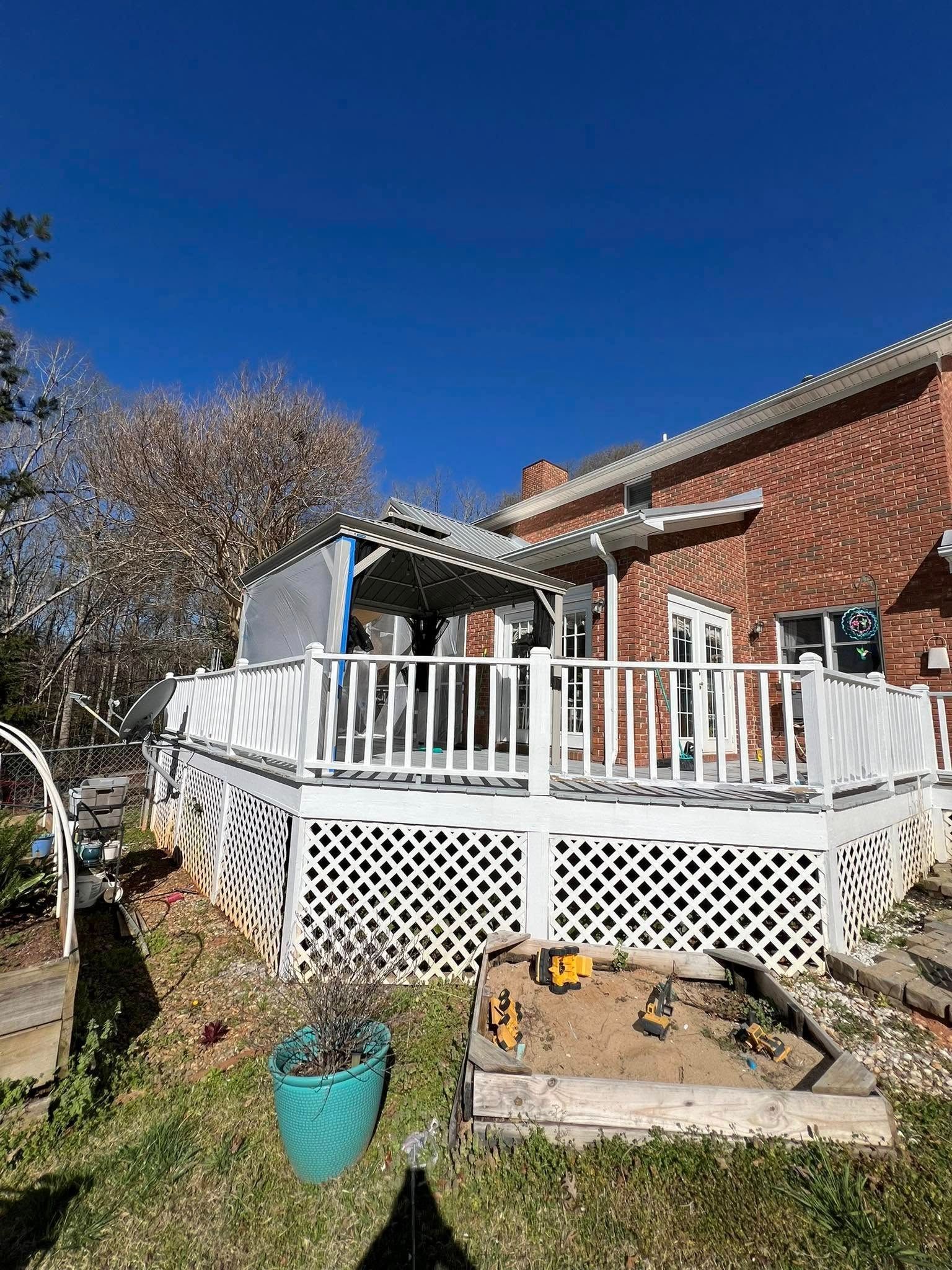 White deck with lattice and railings adjoins a brick house under a blue sky.