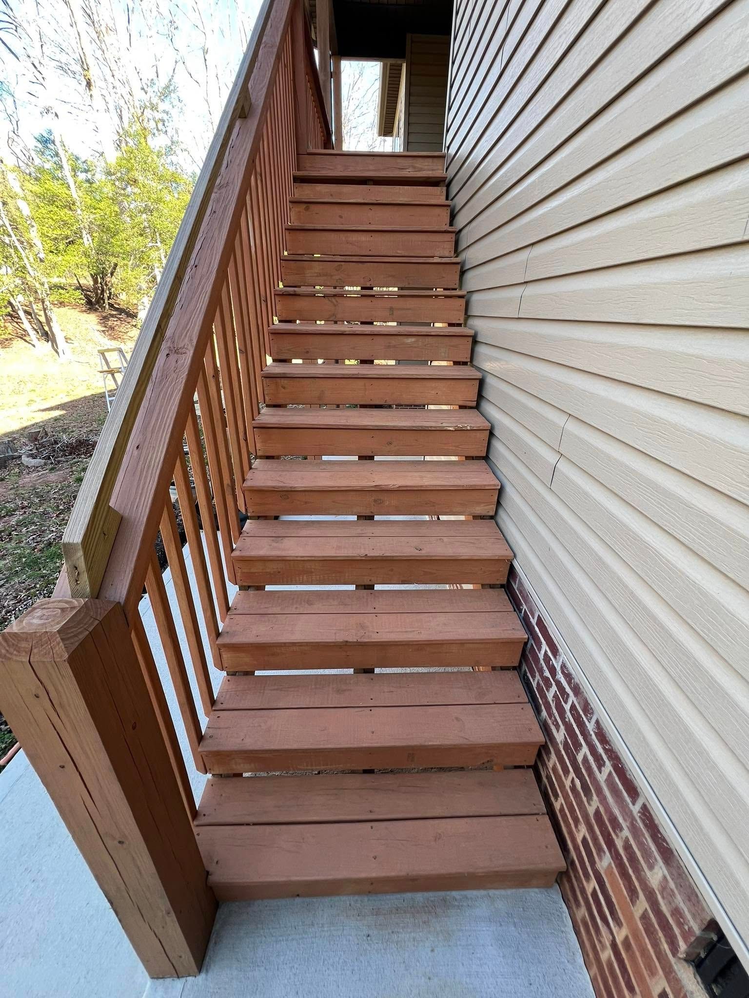 Wooden staircase ascending beside a beige-sided building.