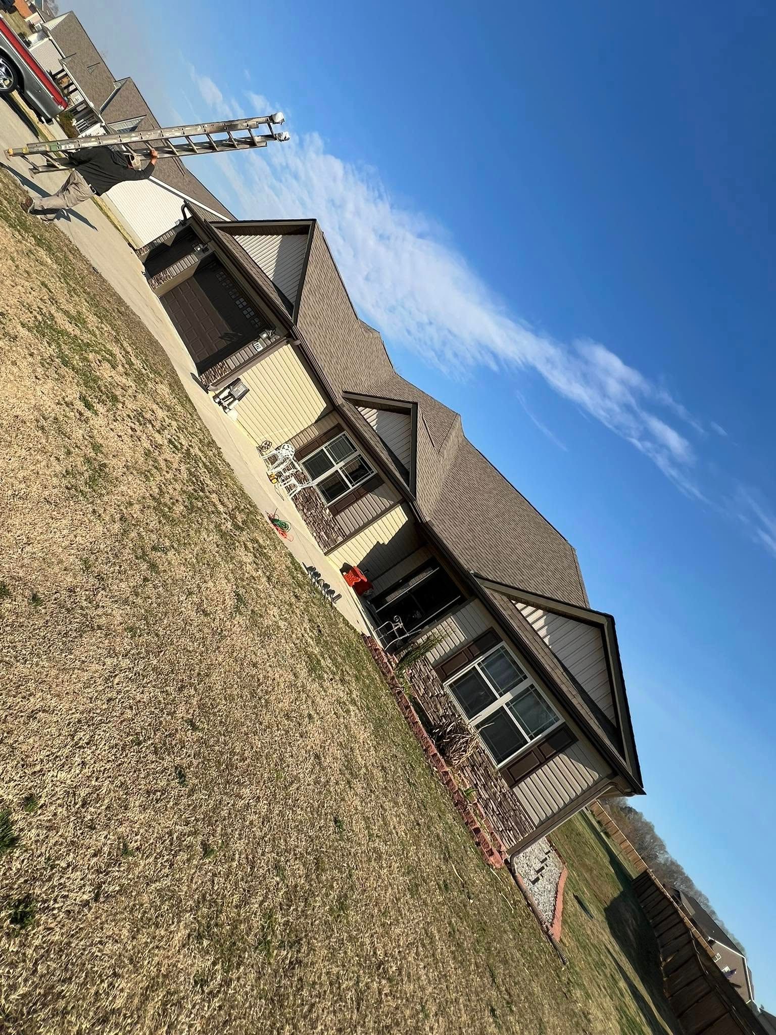 House with brown roof, brick siding, and two windows. A blue sky with whispy clouds.