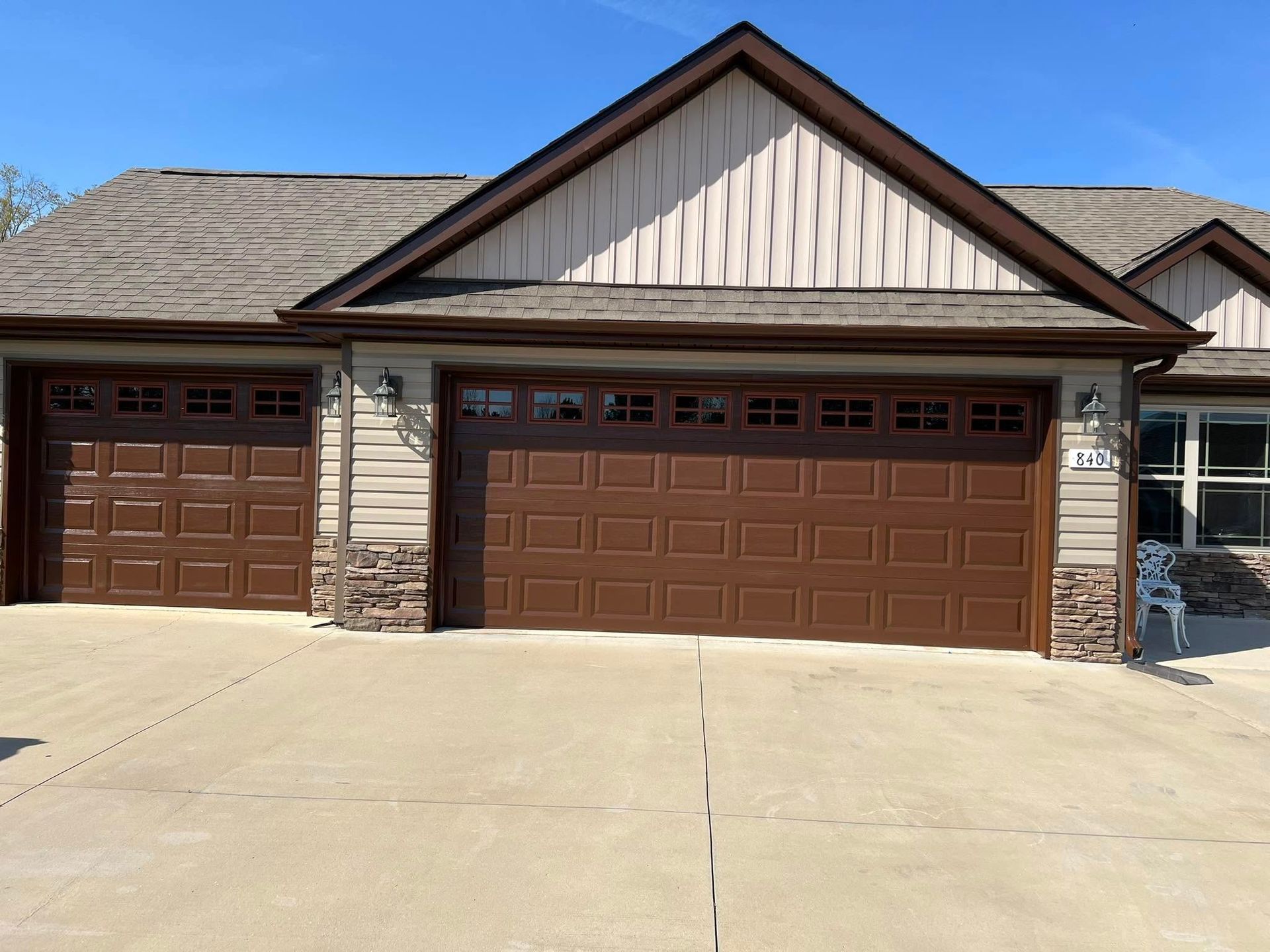 Brown garage doors and tan siding on a house, blue sky.