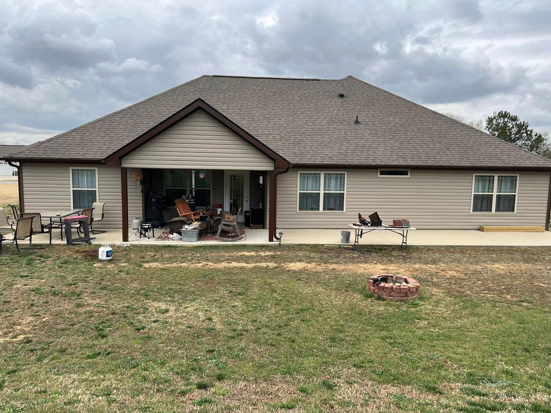 Back of a one-story beige house with a covered patio, outdoor furniture, and a fire pit in the yard.