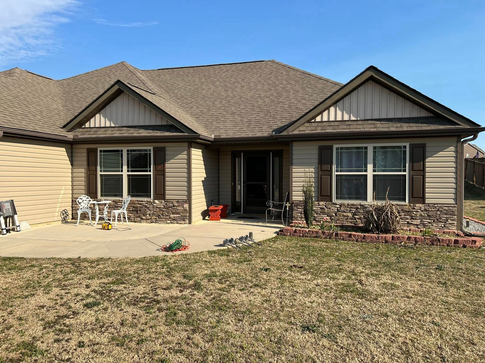 Tan house with brown shutters, porch, and yard. Blue sky.