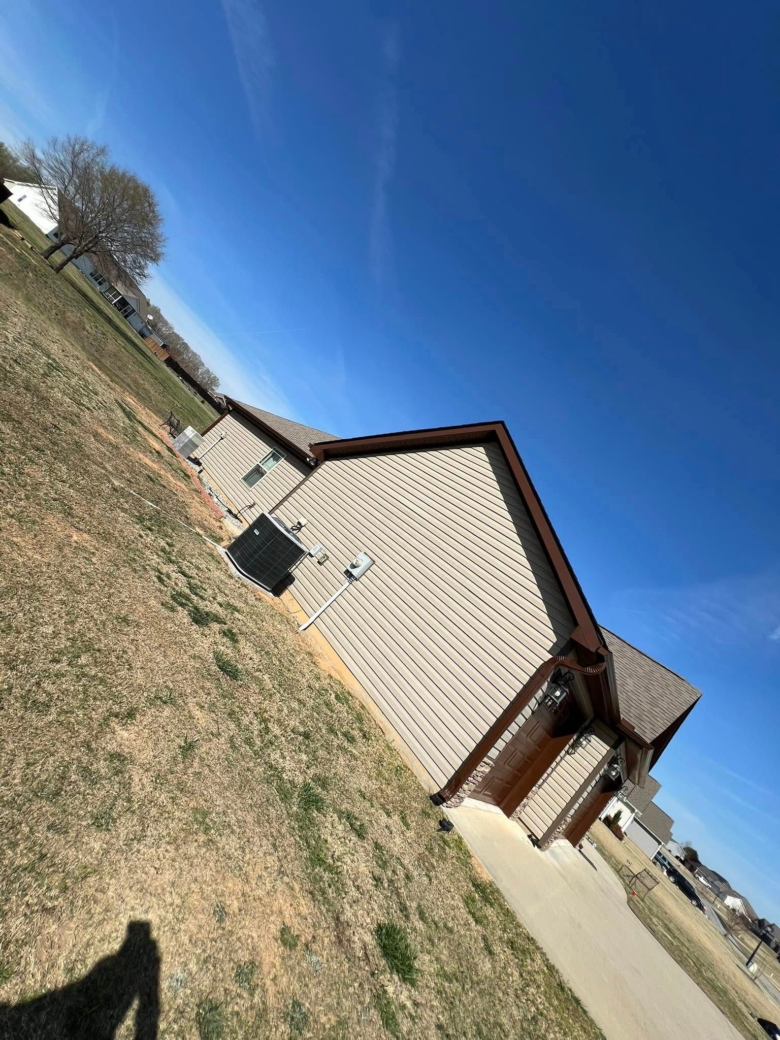 Tan house with a patterned facade, brown roof, against a clear blue sky.