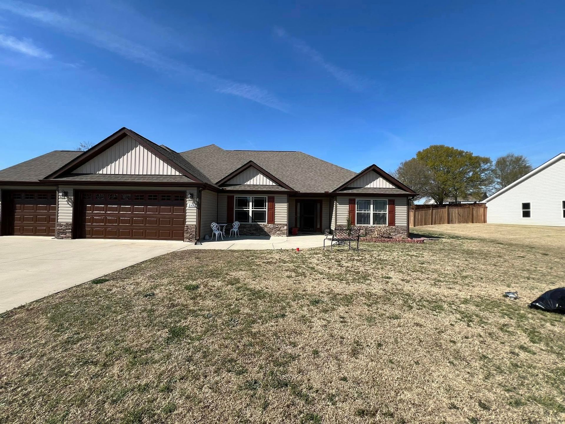 A one-story house with brown garage doors, stone accents, and a brown roof under a blue sky.
