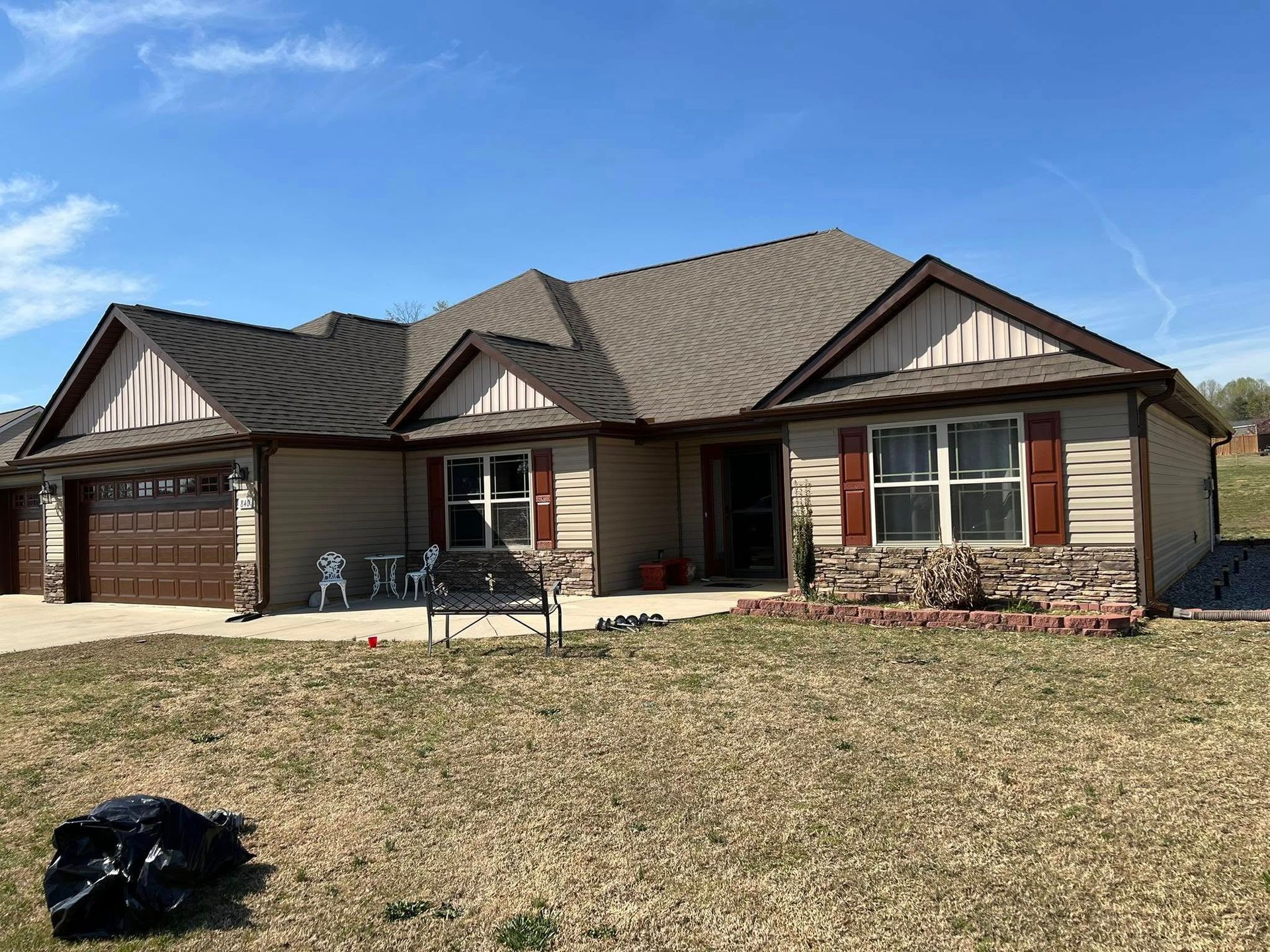 Tan house with brown roof, garage, shutters, and stone accents on a sunny day.