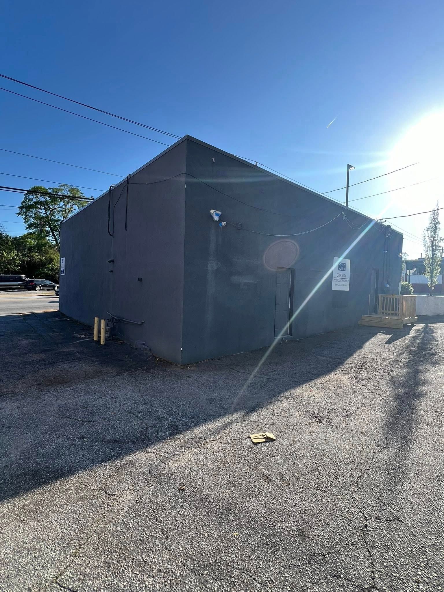Dark gray building with a gravel lot under a bright blue sky.