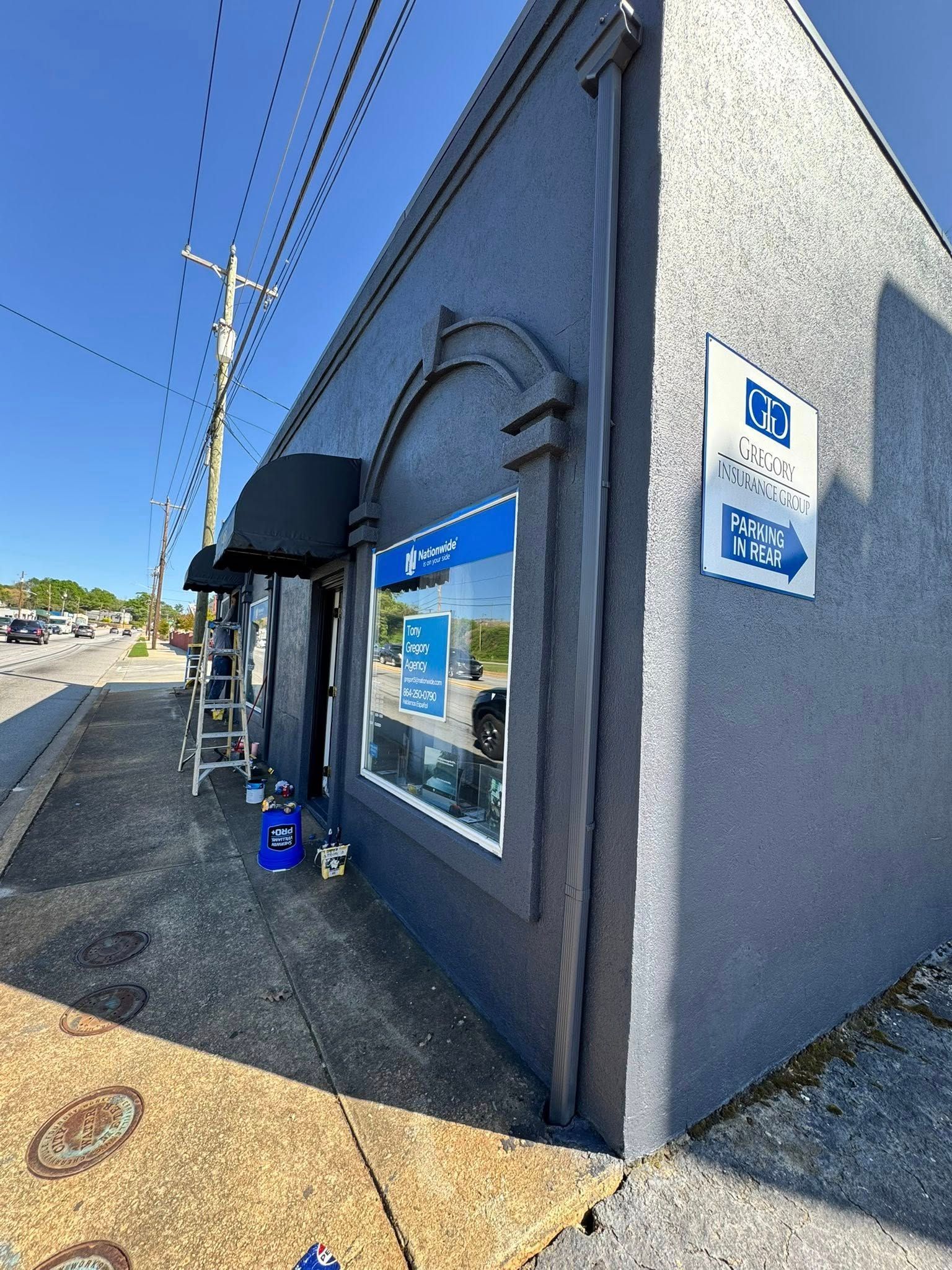 Gray building with awning, storefront window, sign, and sidewalk. Blue sky overhead.