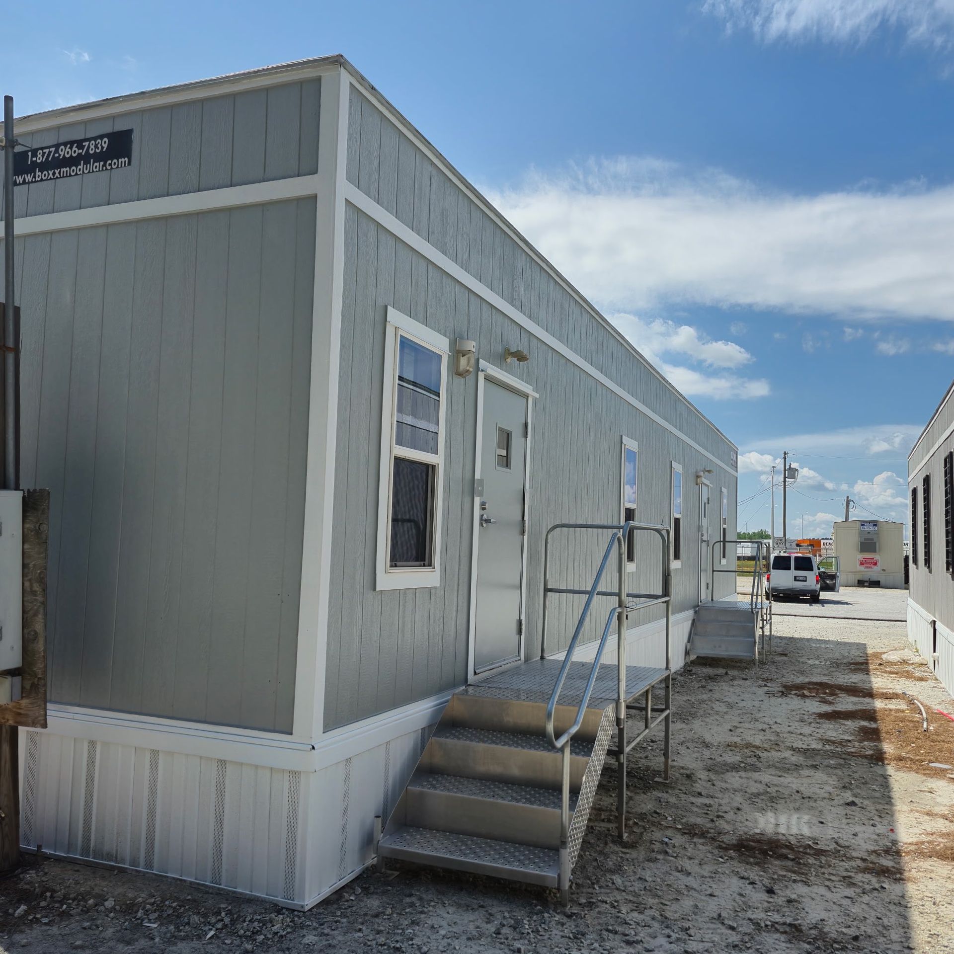 Gray modular building with stairs, a ramp, and a doorway.