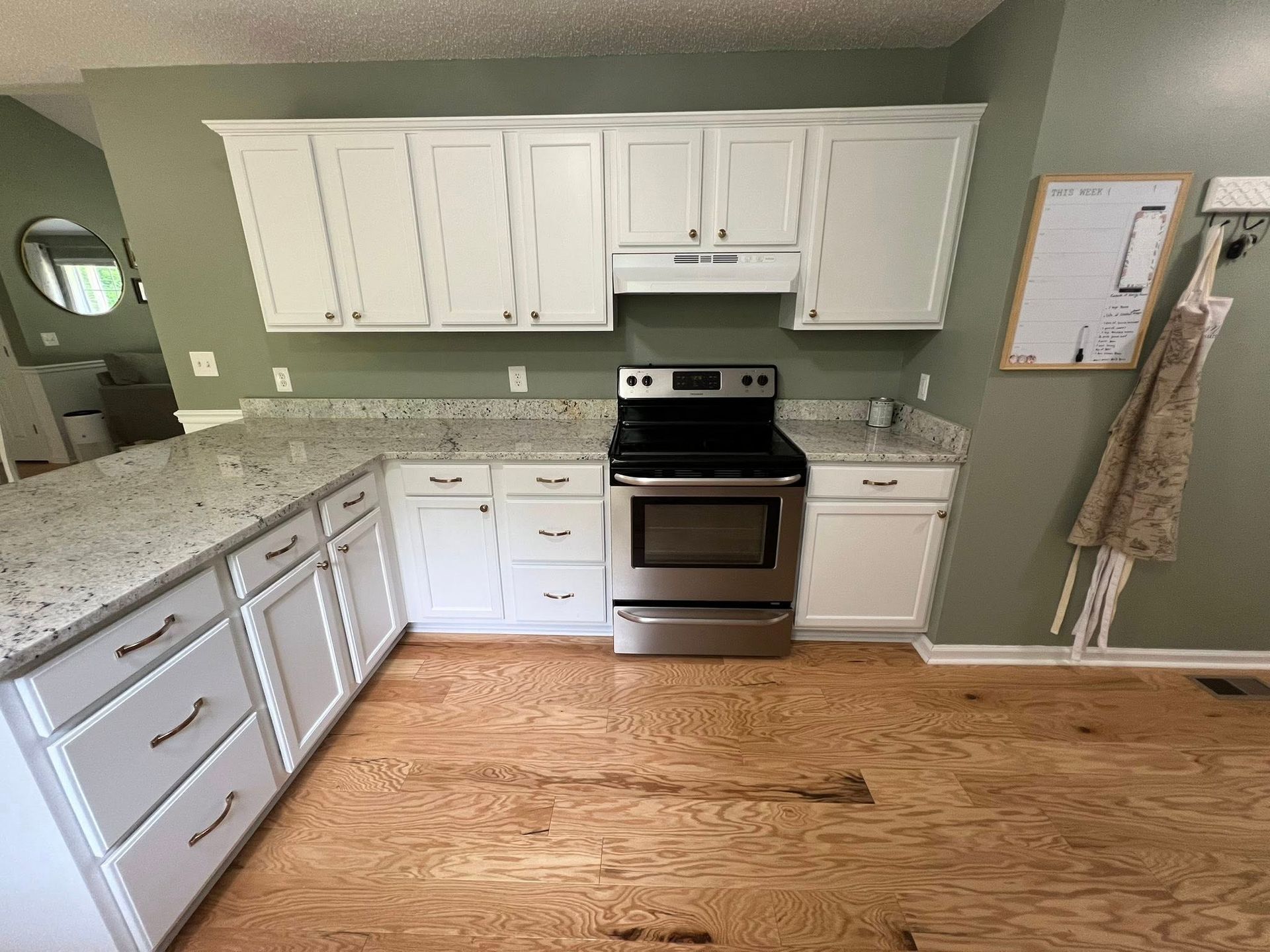 White kitchen with granite countertops and stainless steel appliances; light wood floors.