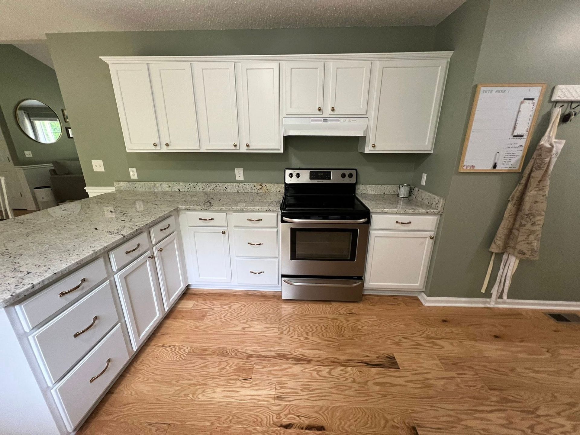 Kitchen with white cabinets, stainless steel oven, and granite countertops. Wooden floors.