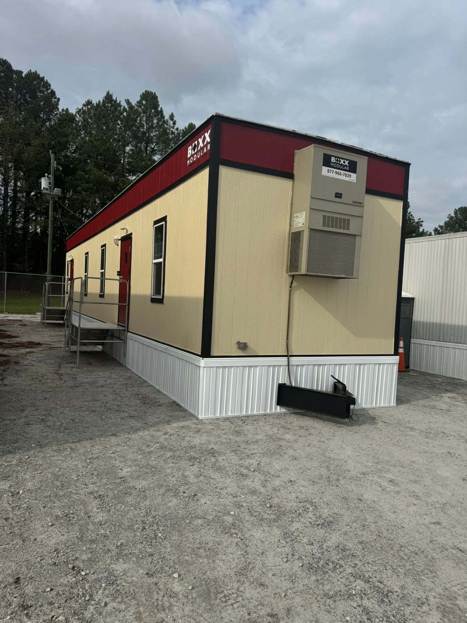 Mobile office building with red trim and air conditioning unit, sitting on gravel.