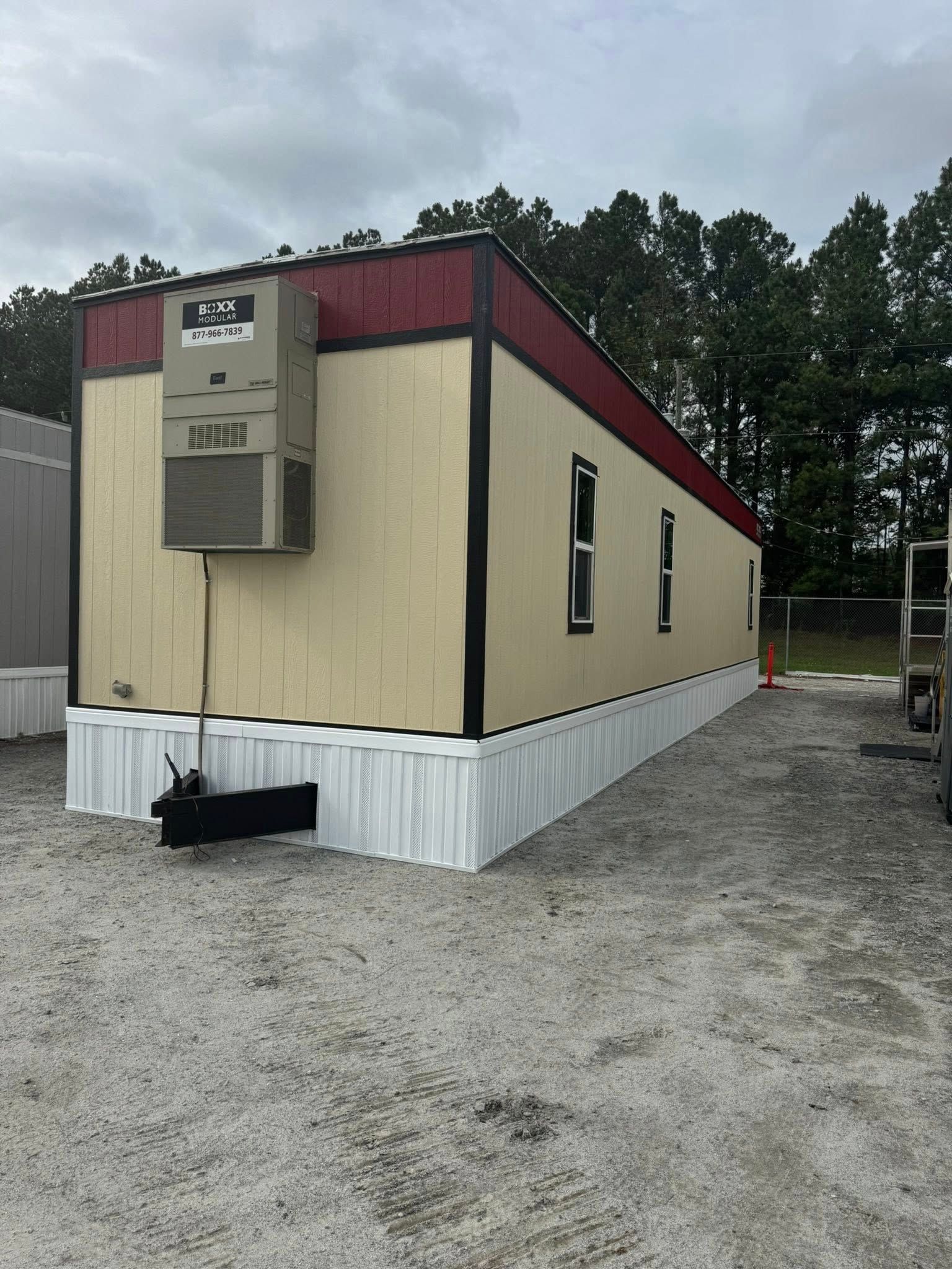 Tan mobile office building with a red roof. Features a trailer hitch and an AC unit on the side.