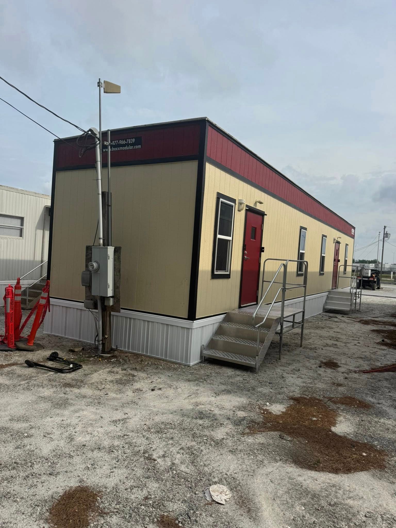 Modular building with a red door and trim, tan siding, and a gray stairway.