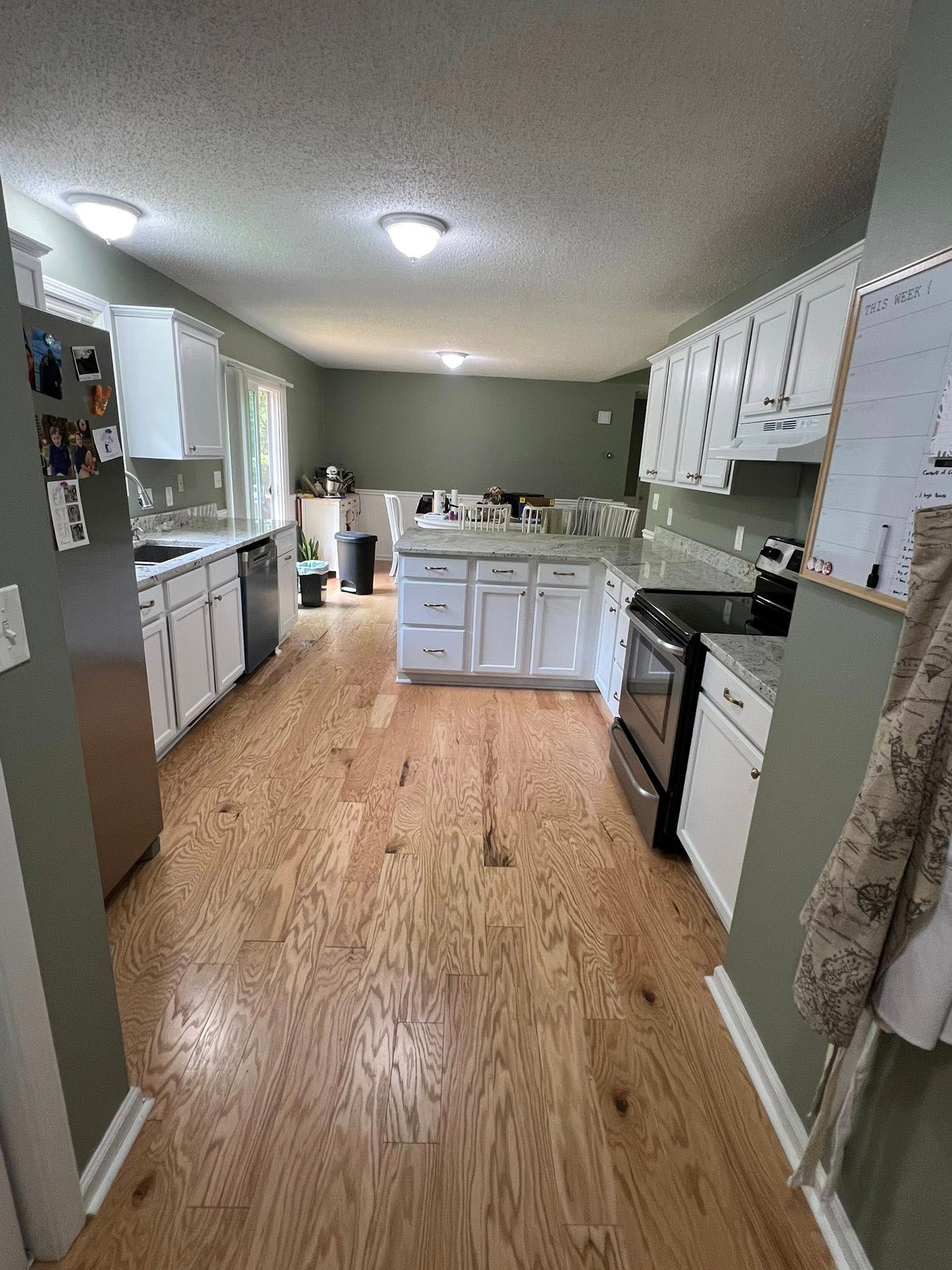 Kitchen with white cabinets, stainless steel appliances, wood floors, and a gray-green wall.