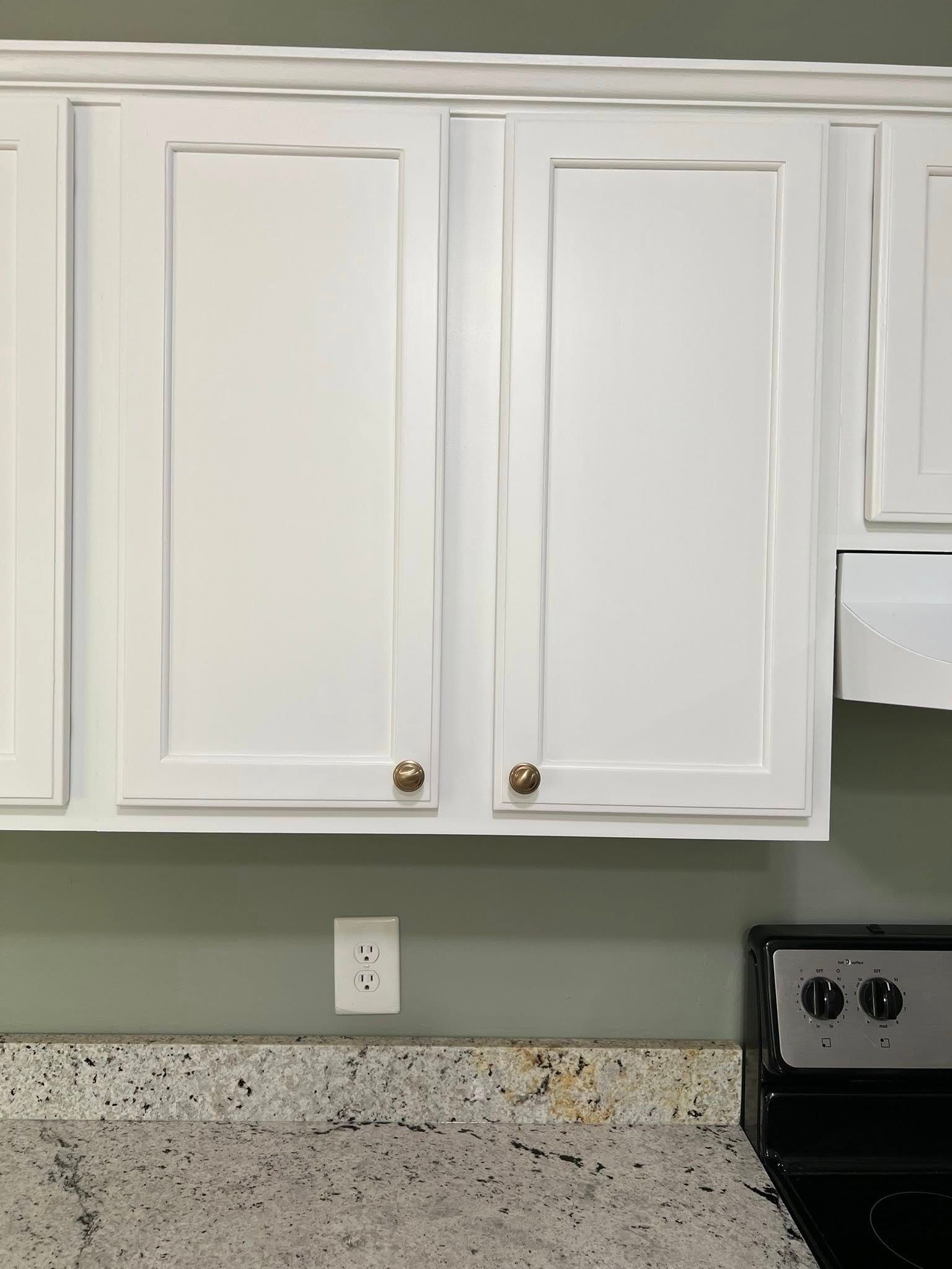 White kitchen cabinets with gold knobs above a speckled countertop.