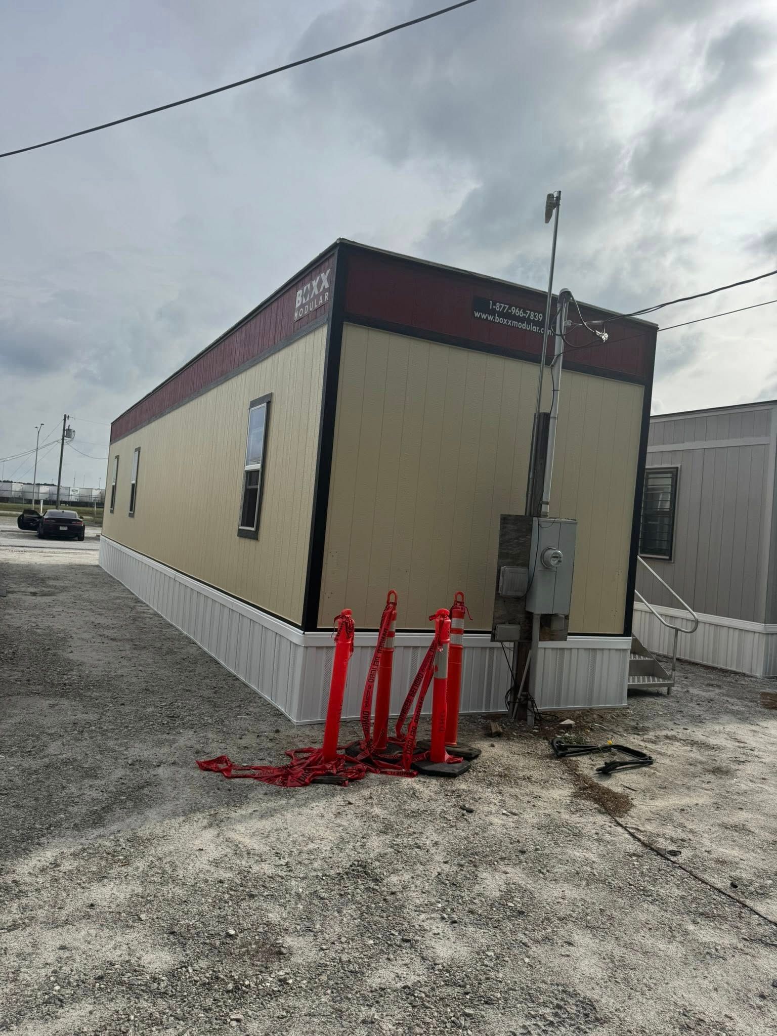 Tan and maroon modular building, surrounded by gravel, with red safety barriers in front.