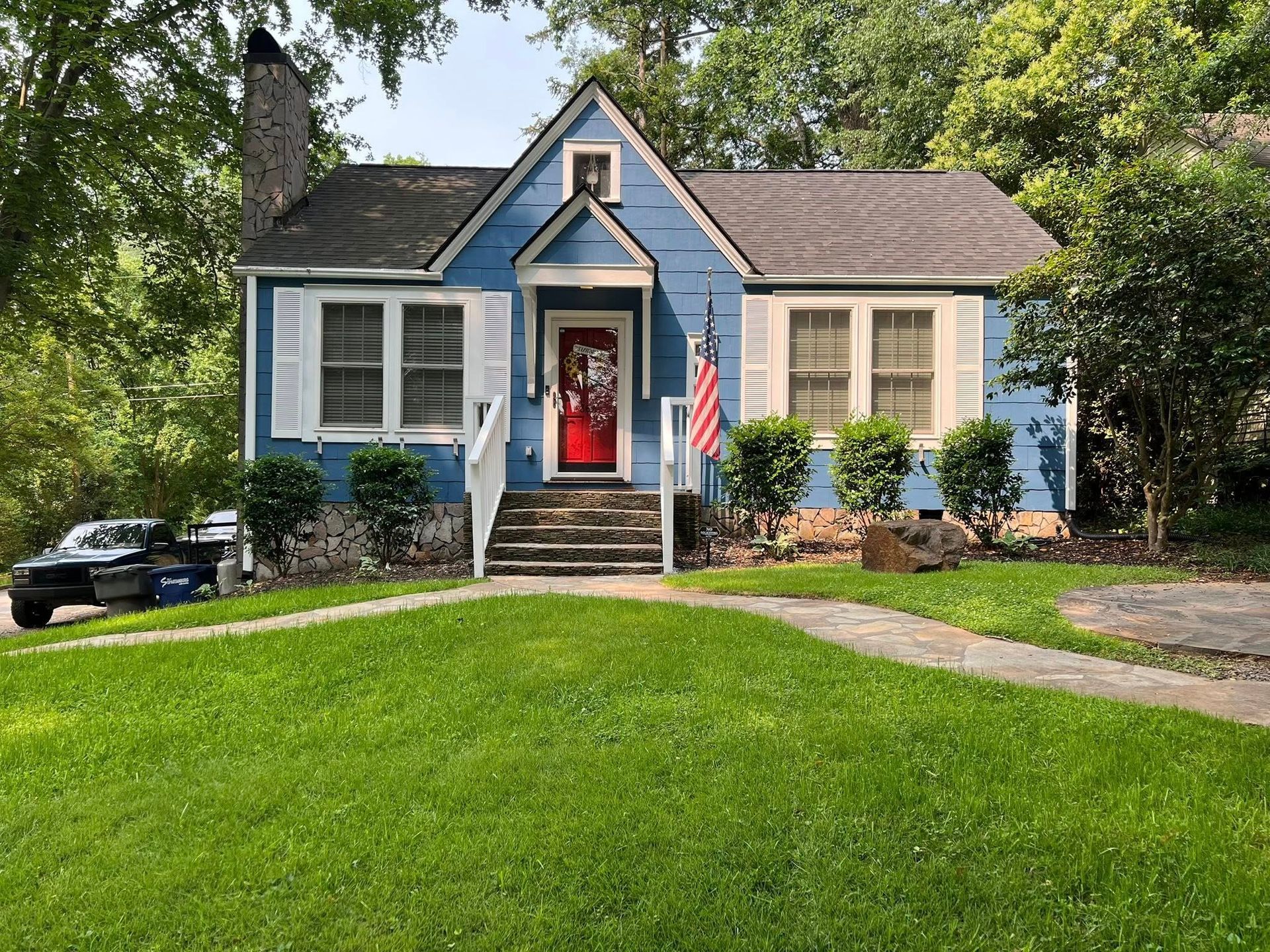Blue cottage with white shutters, red door, American flag, and green lawn.