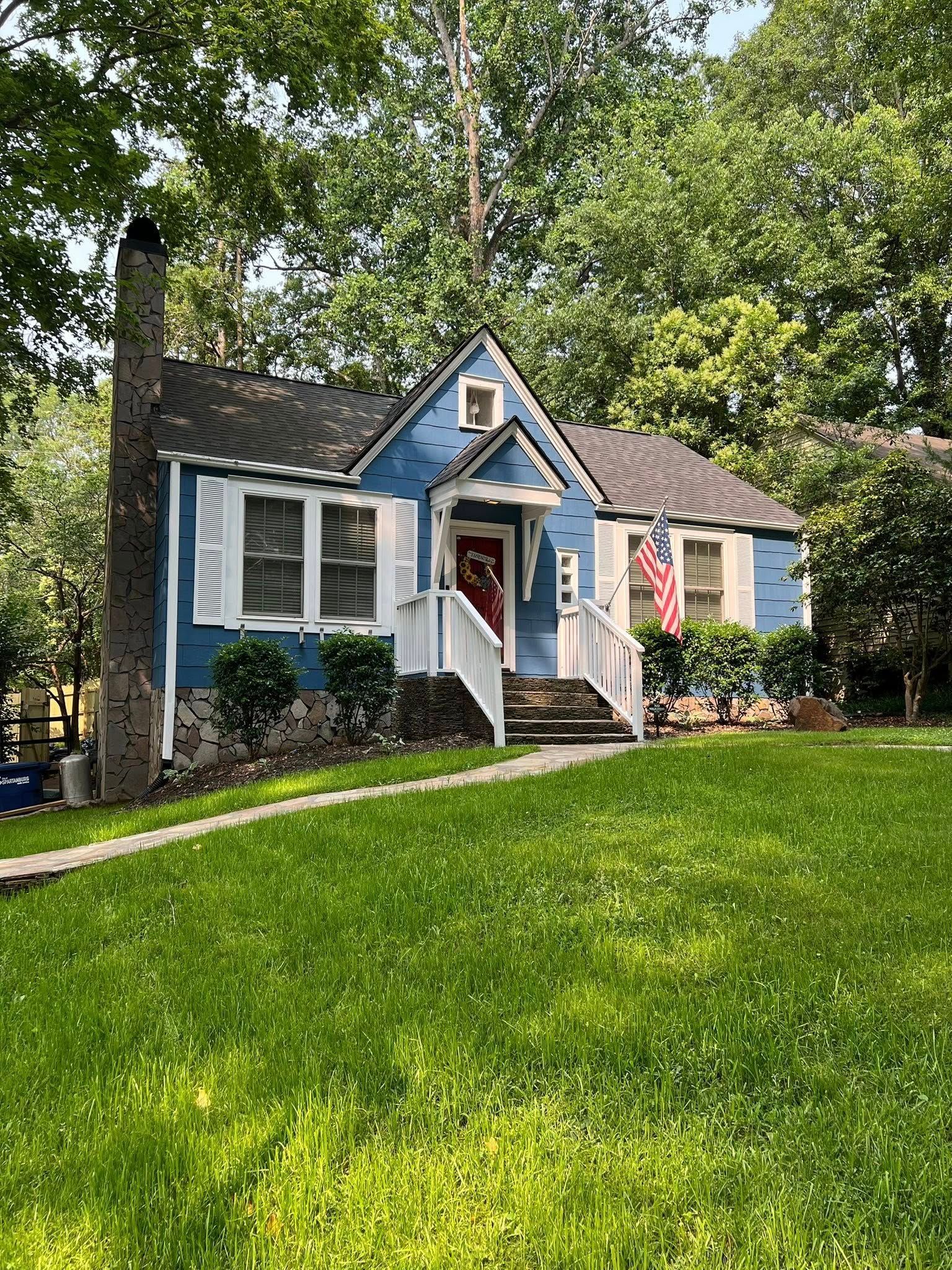 Blue cottage with white shutters, small front porch, American flag, green lawn.
