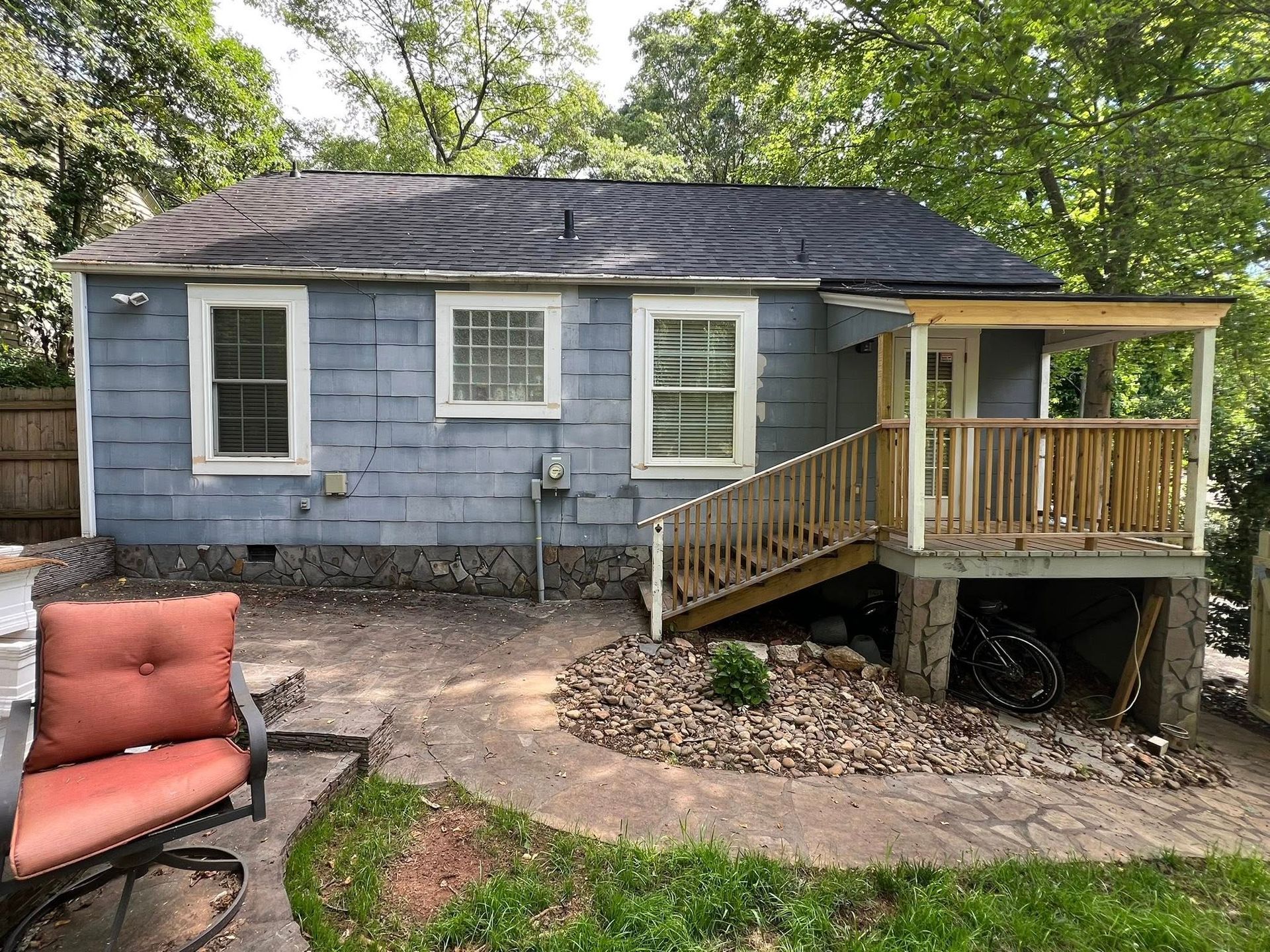 Small blue house with new wooden porch, stairs, and stone path. A red chair sits on the patio.