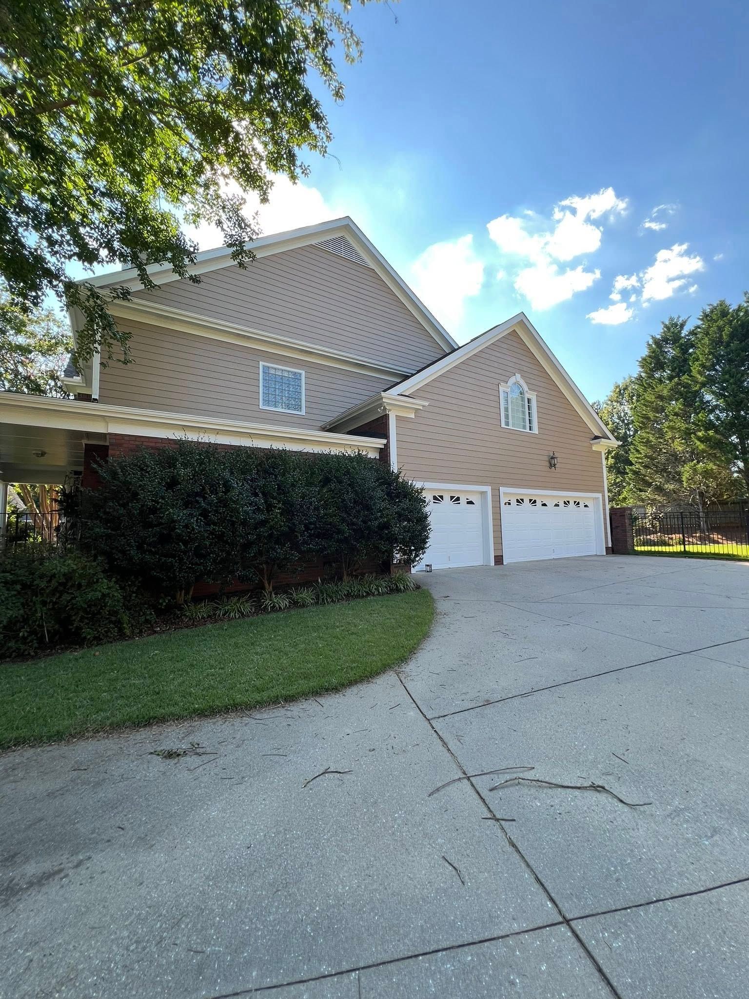 Two-story house with tan siding, white garage doors, and a concrete driveway on a sunny day.