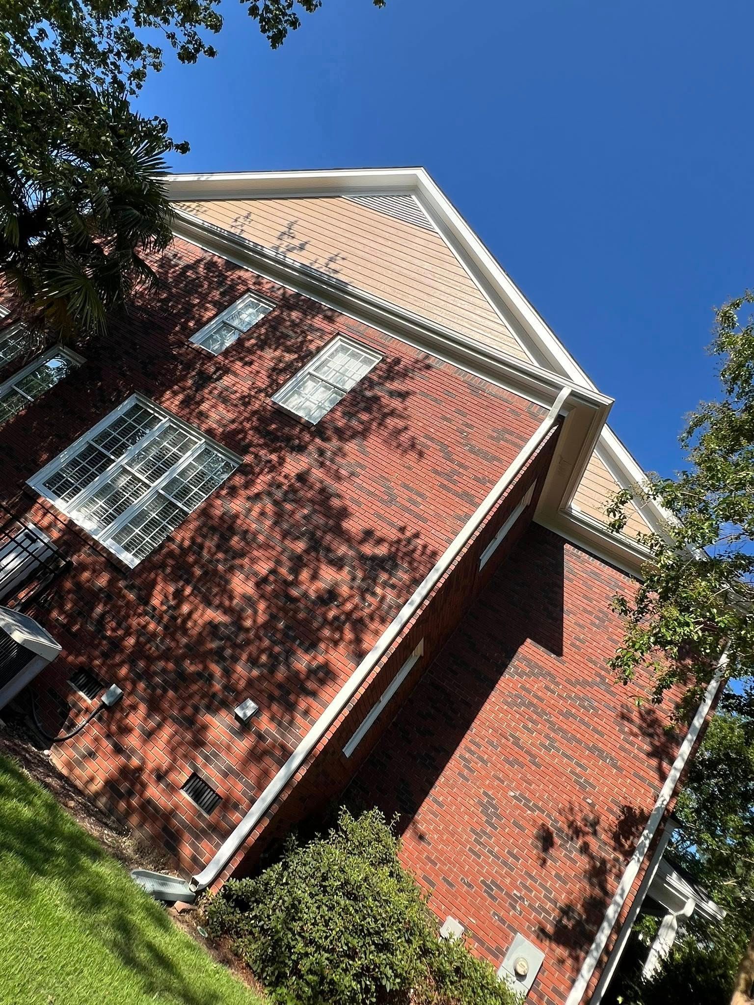 Brick building with white trim and windows against a blue sky. Trees shade the side.