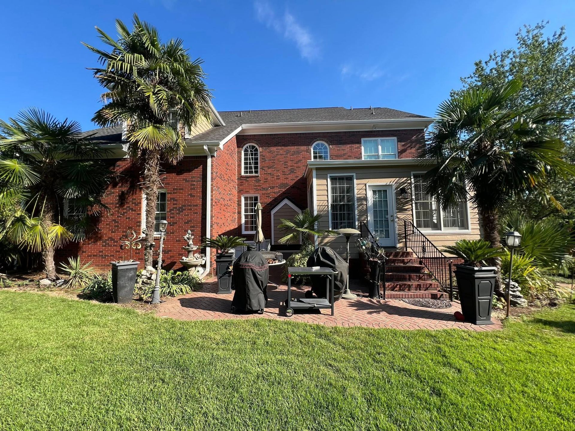 Red brick house with patio, palm trees, and a grassy lawn under a blue sky.