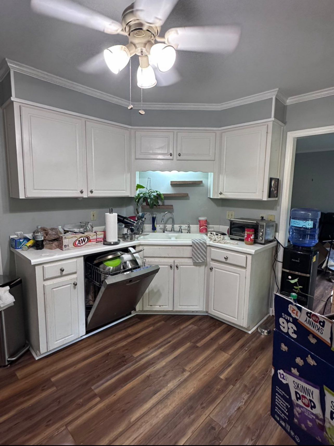Kitchen with white cabinets, open dishwasher, and dark wood floor.