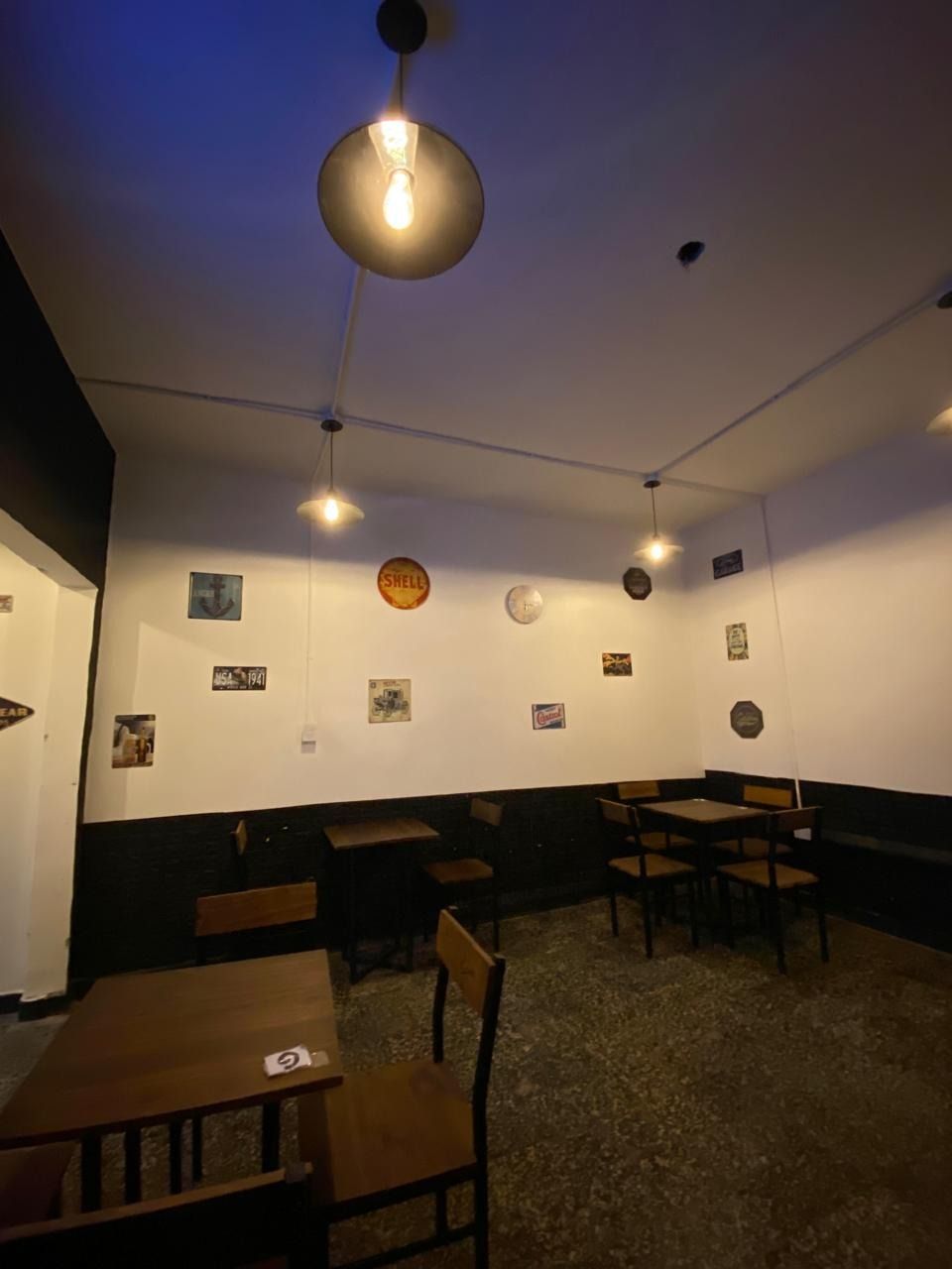 Acogedora zona de estar de cafetería con lámparas colgantes, mesas pequeñas y obras de arte