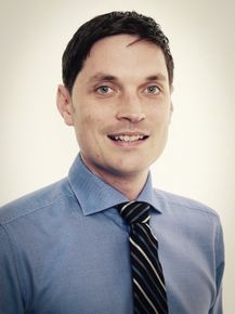 A man in a blue shirt and tie smiles for the camera