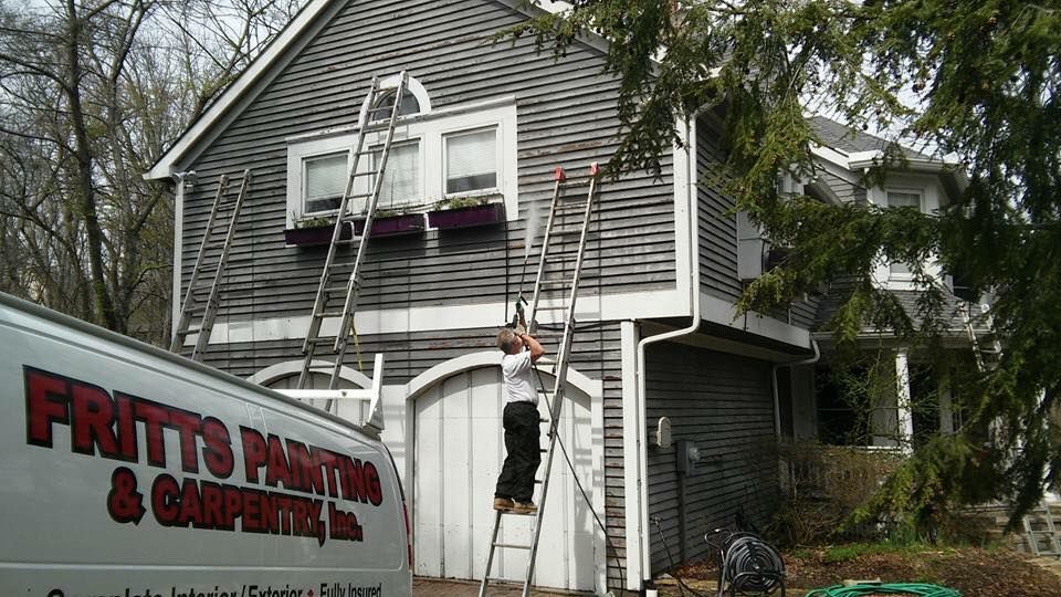 A man standing on a ladder next to a white van that says fritto painting & carpentry