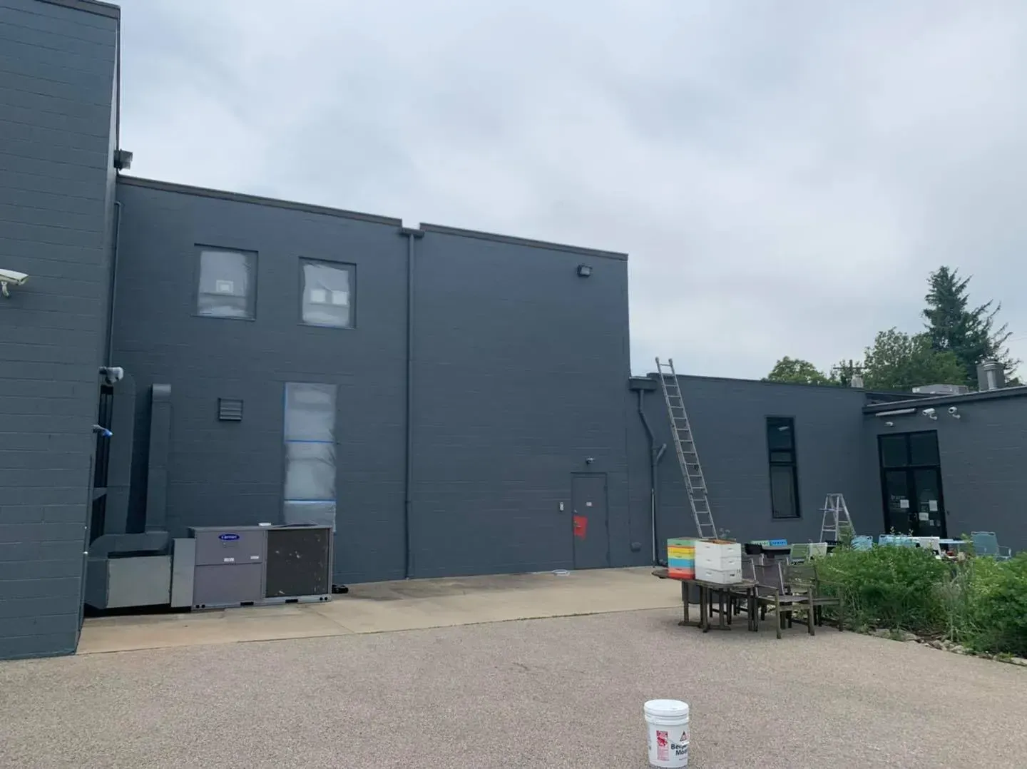A large gray building is being painted on a cloudy day.
