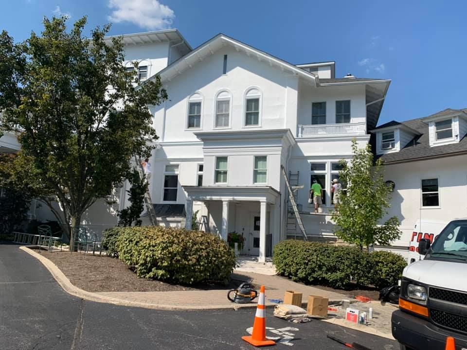 A large white house is being painted on a sunny day.