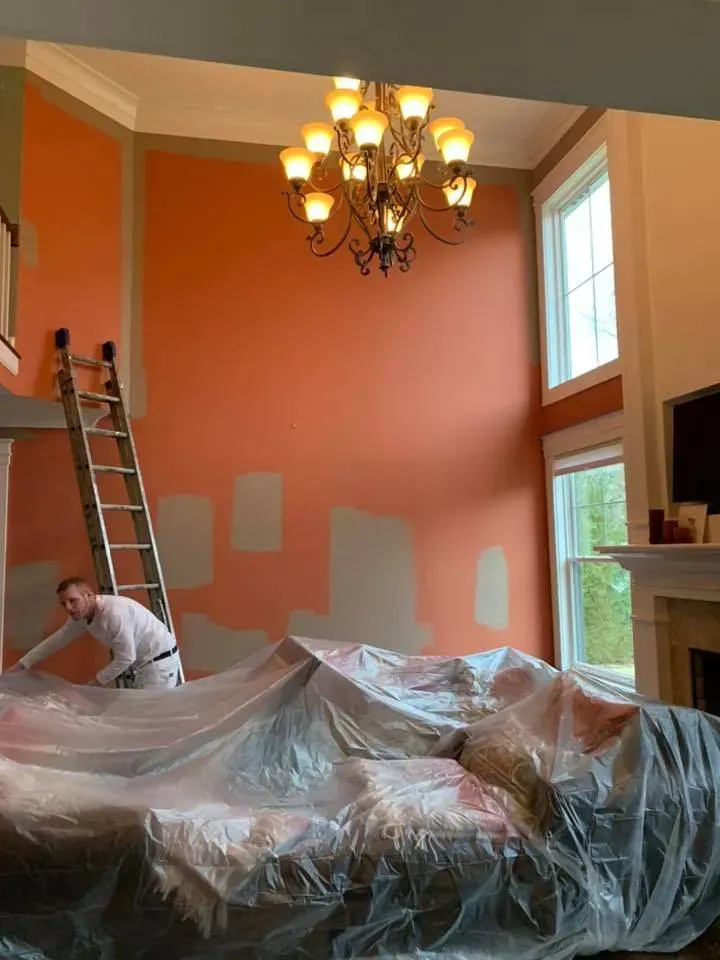 A man is painting a living room with a ladder.