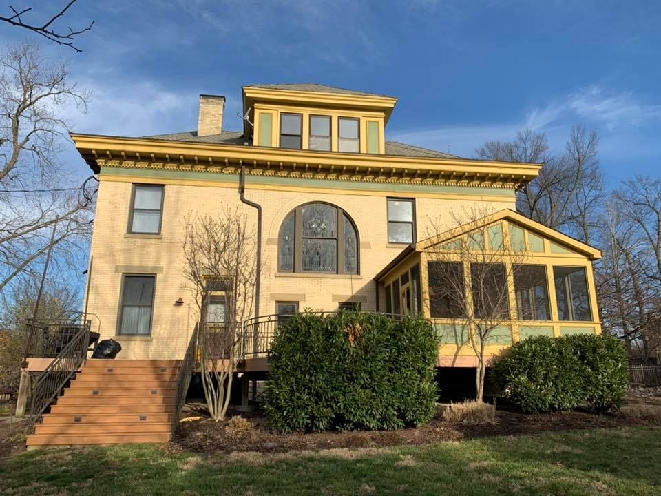 A large yellow house with a screened in porch and stairs