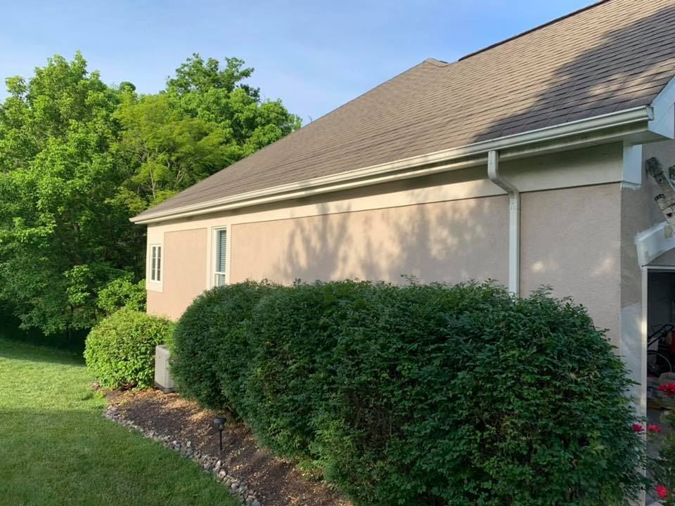 A house with a roof and a hedge in front of it.