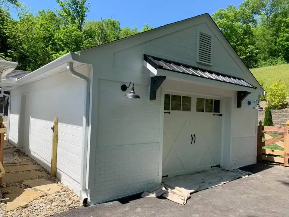 A white garage with a black roof is sitting on top of a hill.