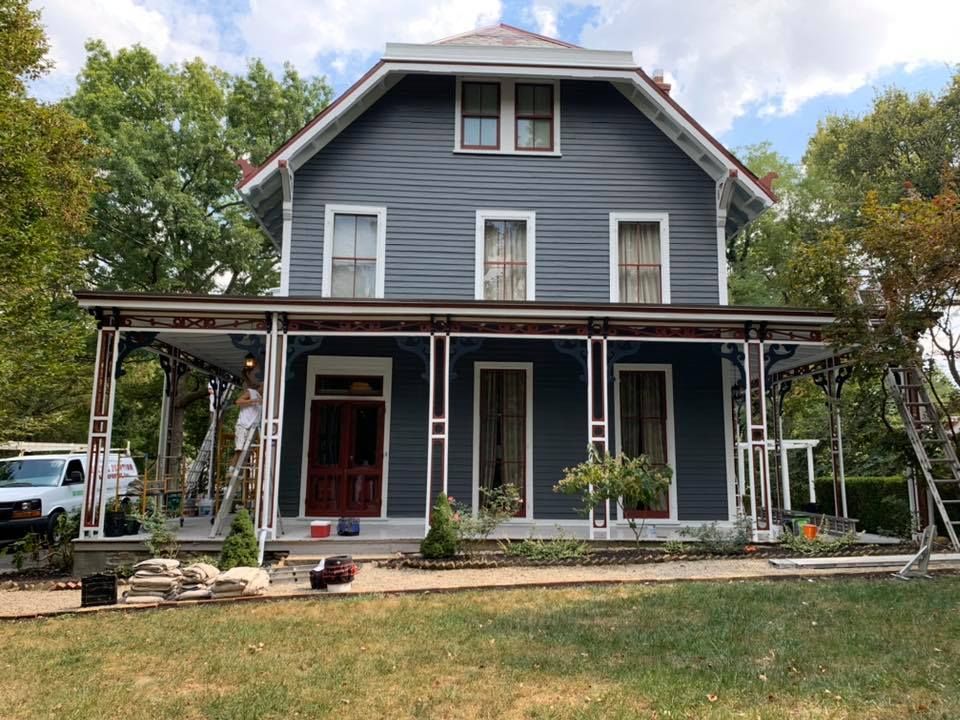 A large blue house with a porch is being painted.