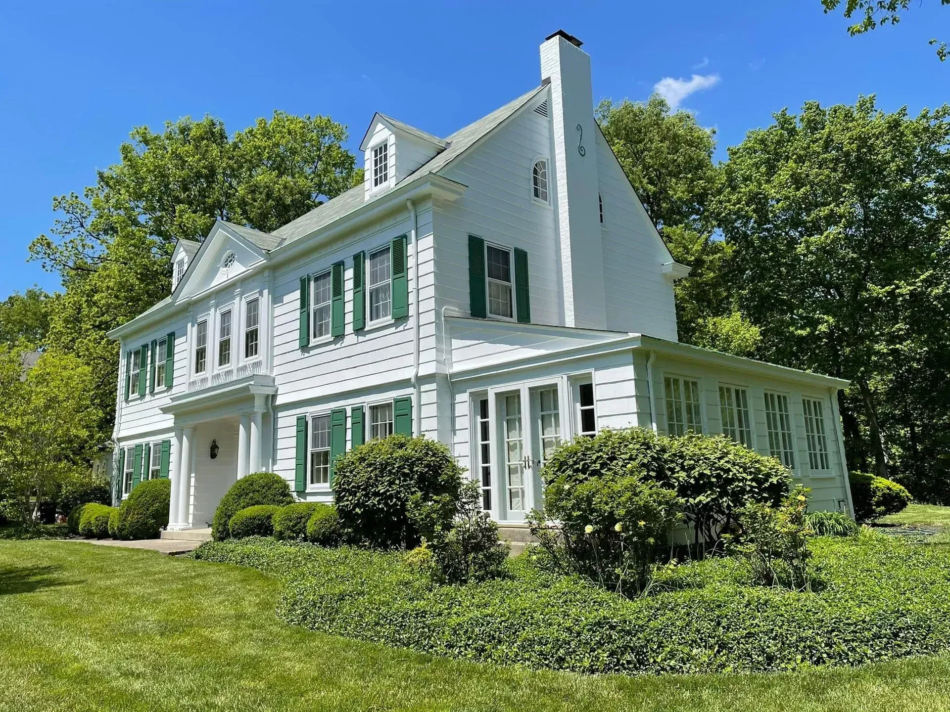A large white house with green shutters and a large lawn in front of it.