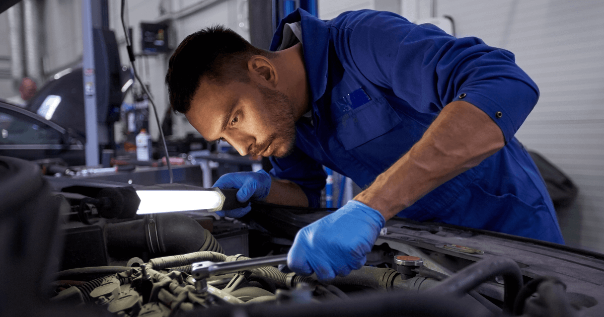 a mechanic under the hod of a car holding a light